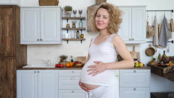 Embarazada feliz mujer tocando su vientre, mirando a la cámara y sonriendo . — Vídeos de Stock