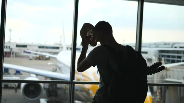 Турист-мужчина, стоящий в аэропорту и смотрящий на самолеты — стоковое видео