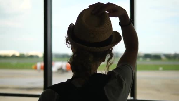 Junge Frau mit Strohhut am Flughafen beim Anblick eines Flugzeugs — Stockvideo