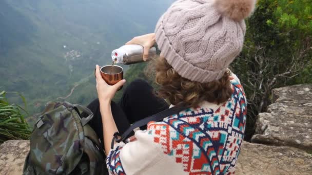 Turista mujer con termo verter té en la taza en un acantilado durante el senderismo — Vídeo de stock