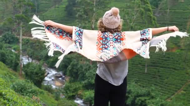 Inspirierende erhebende Frau im Poncho, die Arme vor grünen Hügeln ausbreitet — Stockvideo