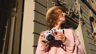Kadın turist, kenti gezerken vintage kamerayla fotoğraf çekiyor.