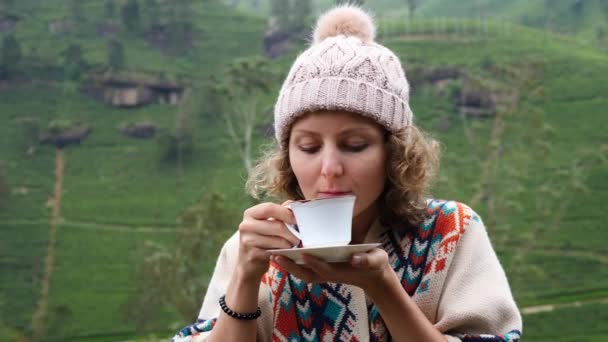 Jonge vrouw in gebreide hoed ruikt thee in de buitenlucht op Tea Plantation Hills — Stockvideo