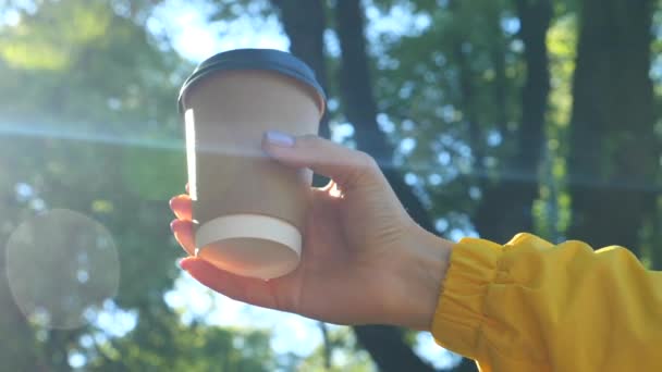 Ruka drží papírový šálek kávy v Sunny Park v dopoledních hodinách — Stock video