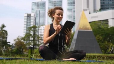 Park 'ta egzersiz yapan genç bir kadın. Yoga yapıyor. Tablet bilgisayar kullanıyor.