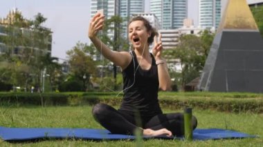 Genç sporcu kadın parkta yoga yaptıktan sonra Smartphone ile selfie çekiyor.
