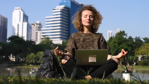 Joven freelancer mujer haciendo meditación en el parque con el ordenador portátil — Vídeos de Stock