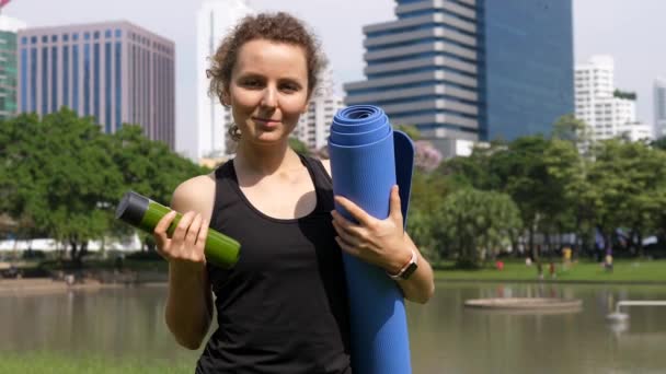 Retrato de mujer joven con esterilla de yoga y batido vegano verde en el parque . — Vídeos de Stock