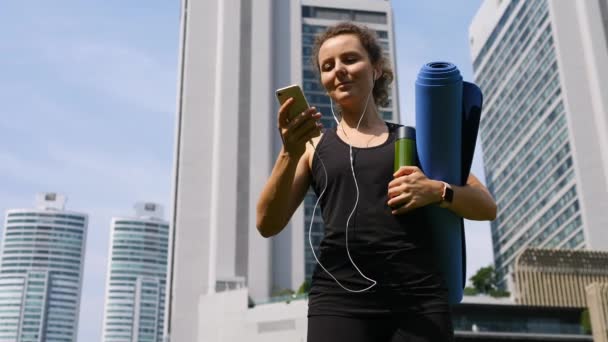 Spor Kadını Yoga Mat ve Yeşil Meyve Smoothie ile Şehir Parkı 'nda Akıllı Telefon Kullanıyor. — Stok video