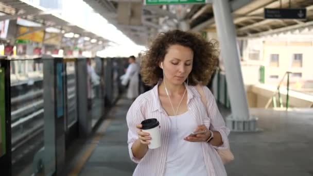 기차역 승강장을 걷고 있는 젊은 여자와 스마트폰을 사용하고 있는 모습 — 비디오