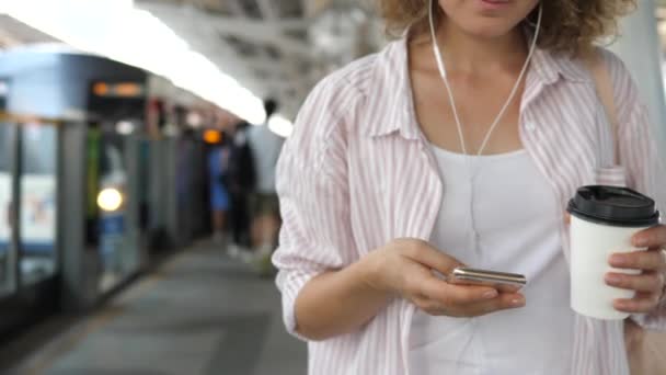 Hipster fille avec café pour aller en utilisant Smartphone sur la plate-forme en attente de train — Video