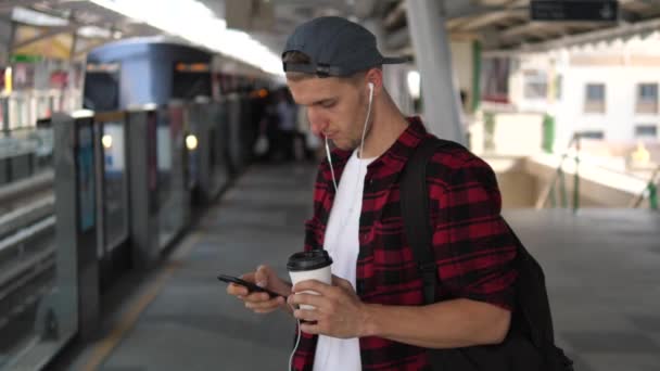 Flanel tişörtlü hippi platformda akıllı telefon kullanarak tren bekliyor. — Stok video