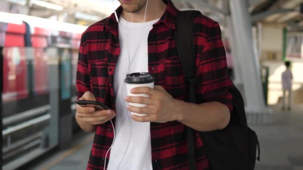 Uomo utilizzando Smart Phone e tenendo tazza di caffè in attesa di treno in città — Video Stock