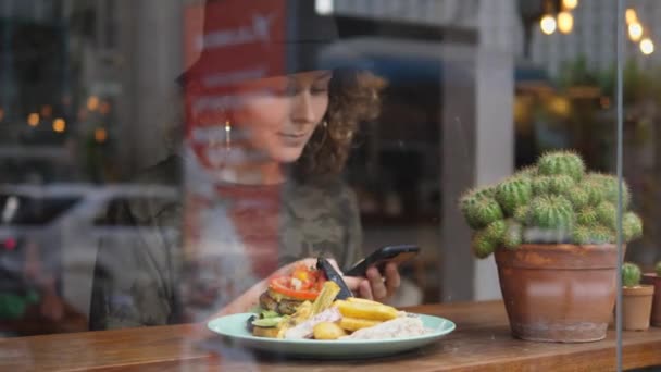 Молодая женщина за ужином в кафе со смартфоном — стоковое видео