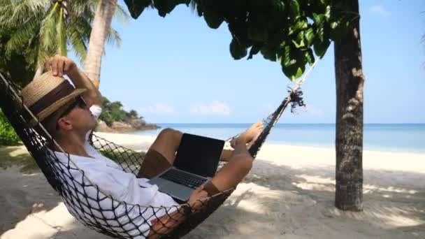 Kumsalda dizüstü bilgisayarla hamakta dinlenen bir iş adamı. — Stok video