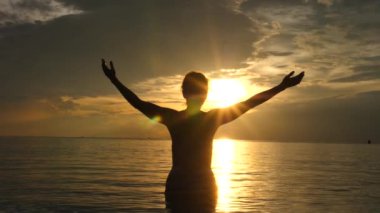 Motivasyon yükseltici kavram. Denizde gün batımında kollarını kaldırmış bir kadın..