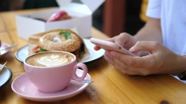 Close Up Of Womans Hands Using Mobile Smart Phone Sitting In Cafe With Cup Of Coffee