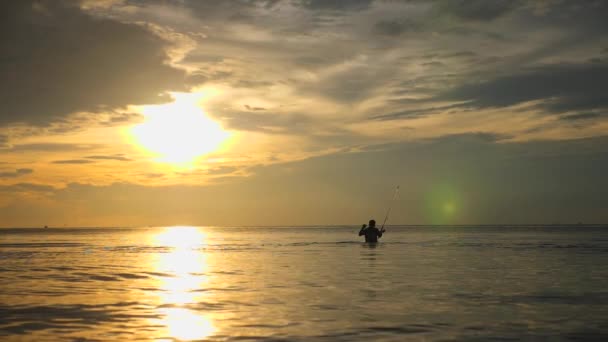 Рыбак рыбачит с удочкой в море на закате — стоковое видео