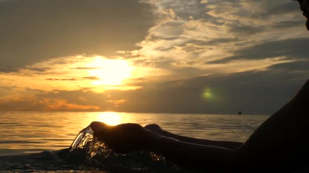 Mains féminines avec de l'eau dans la mer au coucher du soleil. Mouvement lent . — Video