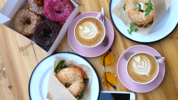 Blick von oben auf das Essen auf dem Holztisch zum Frühstück. Kaffee, Donuts und Bagels. — Stockvideo