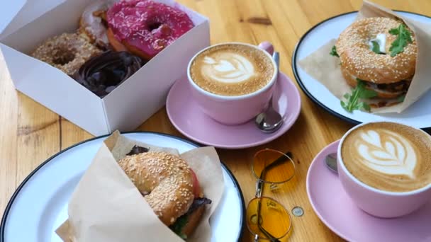 Desayuno de moda con rosquillas, rosquillas y café en mesa de madera — Vídeo de stock