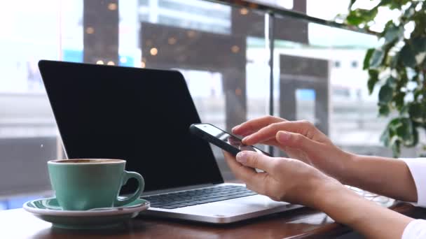Γυναίκα χέρια χρησιμοποιώντας Smartphone, ενώ κάθεται με το laptop στο καφέ — Αρχείο Βίντεο