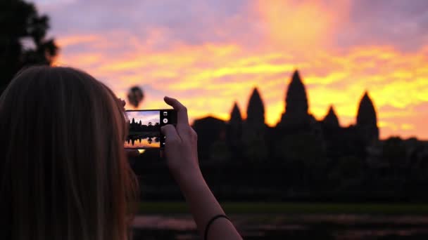 Kobieta robi zdjęcie z telefonu Angkor o wschodzie słońca podczas zwiedzania — Wideo stockowe