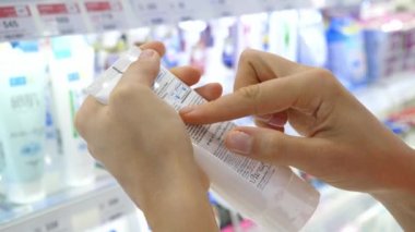 Kadın müşteri süpermarkette kozmetik şişe etiket okuma