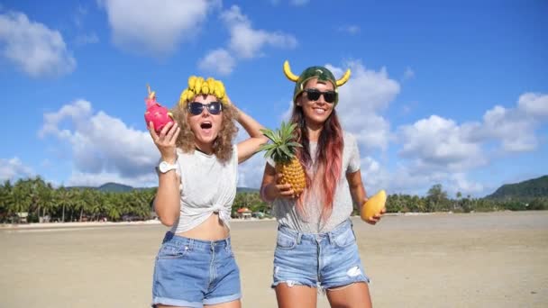 Jóvenes amigas divirtiéndose en la playa bailando con frutas — Vídeo de stock