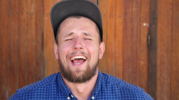 Młody przystojniak śmiejący się z drewnianego muru — Wideo stockowe