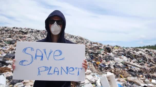 Man met masker roept op om planeet te redden tegen vuilnisbelt — Stockvideo