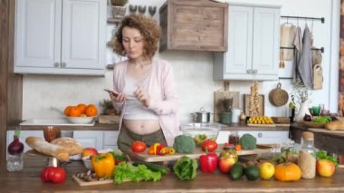 Akıllı telefondan yemek tarifi arayan ve mutfakta salata yapan hamile bir kadın..