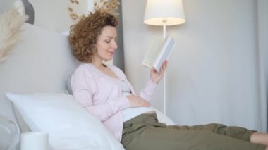 Hamile kadın evde kitapla birlikte yatağında dinleniyor. Mutlu Hamilelik Konsepti.