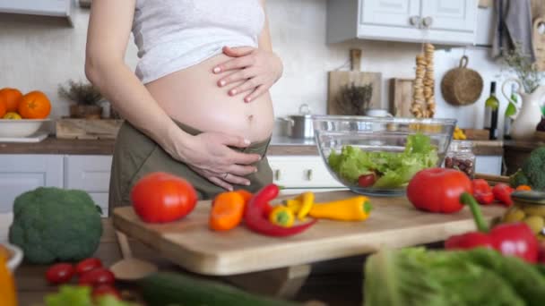 Gros plan de femme enceinte tenant son ventre tout en cuisinant un repas sain . — Video