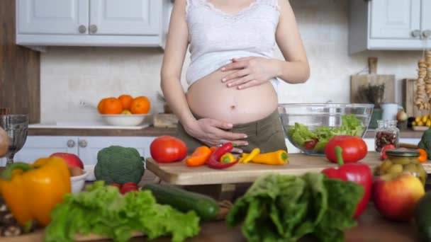 Беременная женщина готовит свежий салат и держит живот на кухне . — стоковое видео