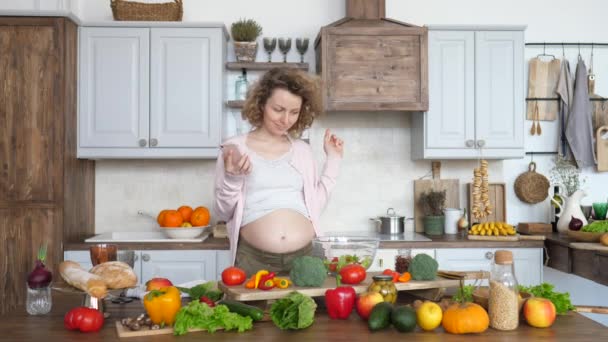 Счастливая беременная женщина готовит здоровую пищу на кухне и с помощью мобильного телефона . — стоковое видео