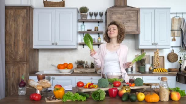 Schöne schwangere Frau bereitet Essen zu und tanzt mit Salat in der Küche. — Stockvideo