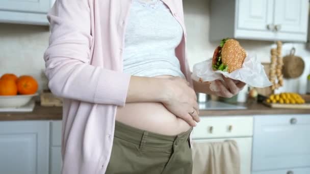 Schwangere mit Bauch hält Burger in der Hand - ungesundes Essen im Schwangerschaftskonzept — Stockvideo