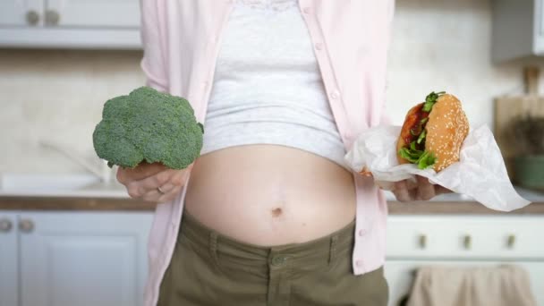 Gezond dieet tijdens de zwangerschap Concept. Zwangere vrouw met hamburger en broccoli. — Stockvideo