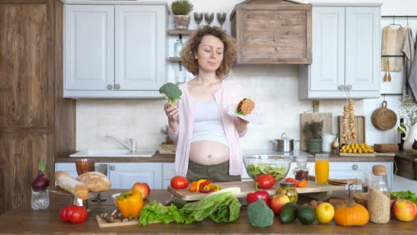 Gravid kvinna som håller Burger och Broccoli bestämma vad du ska äta — Stockvideo