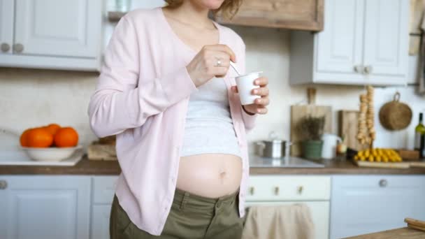 Fiatal terhes nő joghurtot eszik a konyhában. — Stock videók