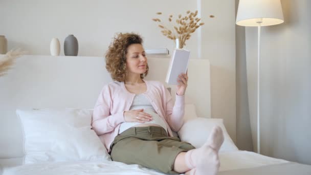 Mujer embarazada descansando en la cama leyendo un libro. Feliz embarazo. . — Vídeos de Stock