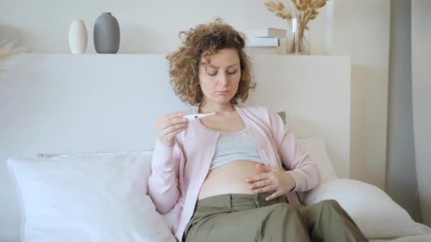 Zwangere vrouw lezen temperatuur op thermometer op bed thuis — Stockvideo