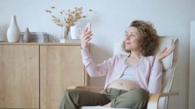 Video görüşmesi yapan ve akıllı telefon kullanarak el sallayan mutlu hamile kadın..