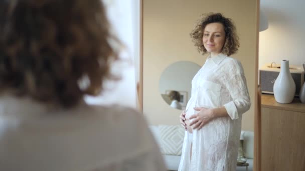 Embarazo, maternidad, personas y concepto de expectativa - mujer embarazada feliz mirando al espejo en casa — Vídeos de Stock