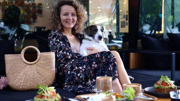 Beautiful Woman Sitting In Cafe With Dog Having Breakfast