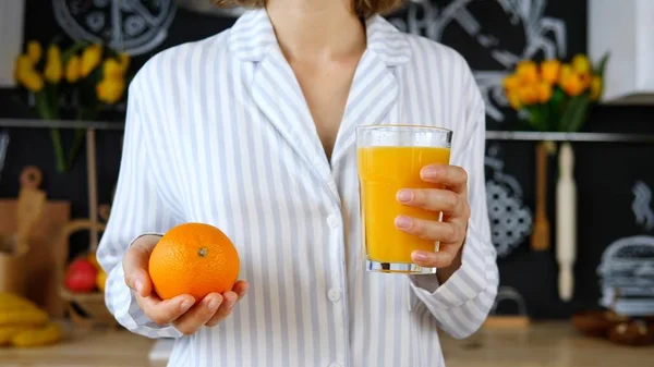 Ung kvinna i Pajamas håller färsk apelsinjuice i handen — Stockfoto