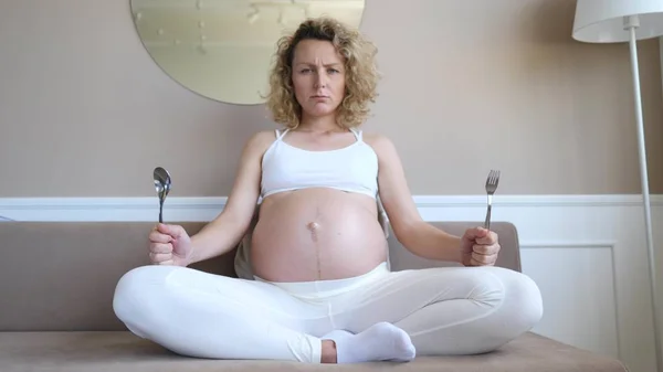 Affamato donna incinta insoddisfatta tenendo cucchiaio e forchetta nelle mani in attesa di cibo . — Foto Stock