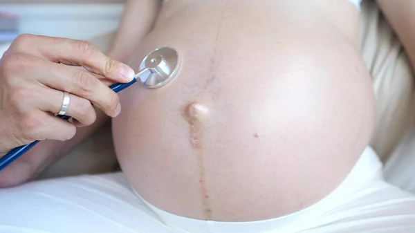 Доктор использует стетоскоп, чтобы услышать живот беременной женщины — стоковое фото