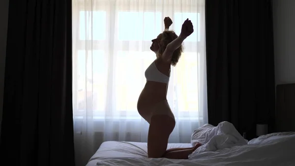 Joven mujer embarazada estirándose y despertando en la cama en casa —  Fotos de Stock